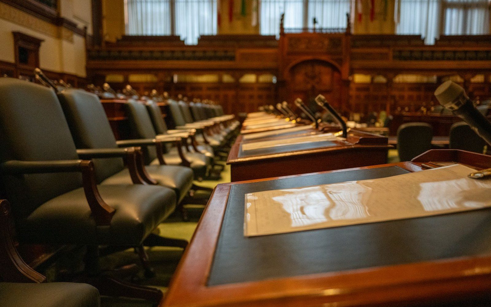 Empty rows of desks and leather chairs in a wood-paneled legislative chamber