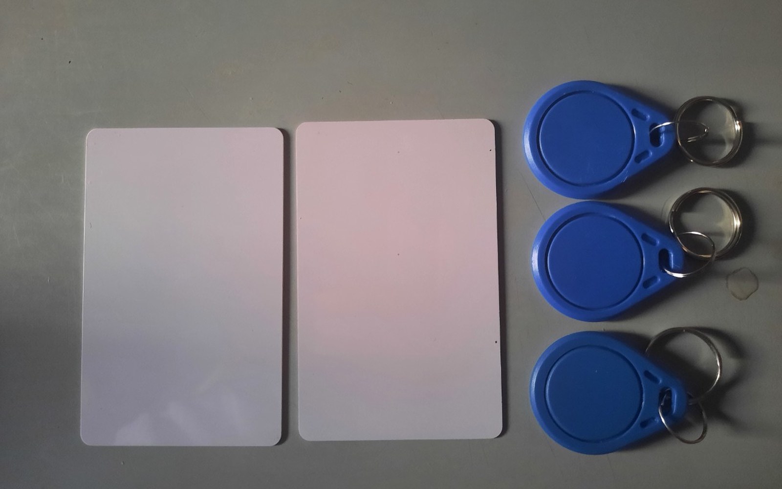 Two blank white access cards beside three blue RFID key fobs on split key rings
