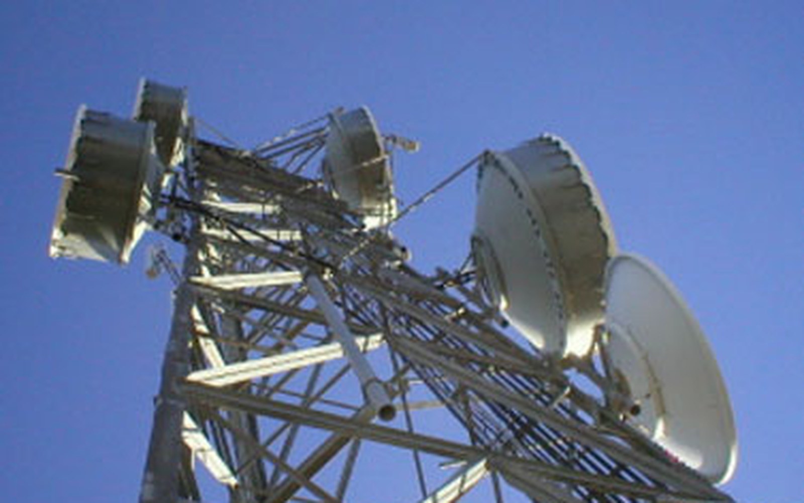 Multiple satellite dishes mounted on a steel telecommunications tower against a clear blue sky