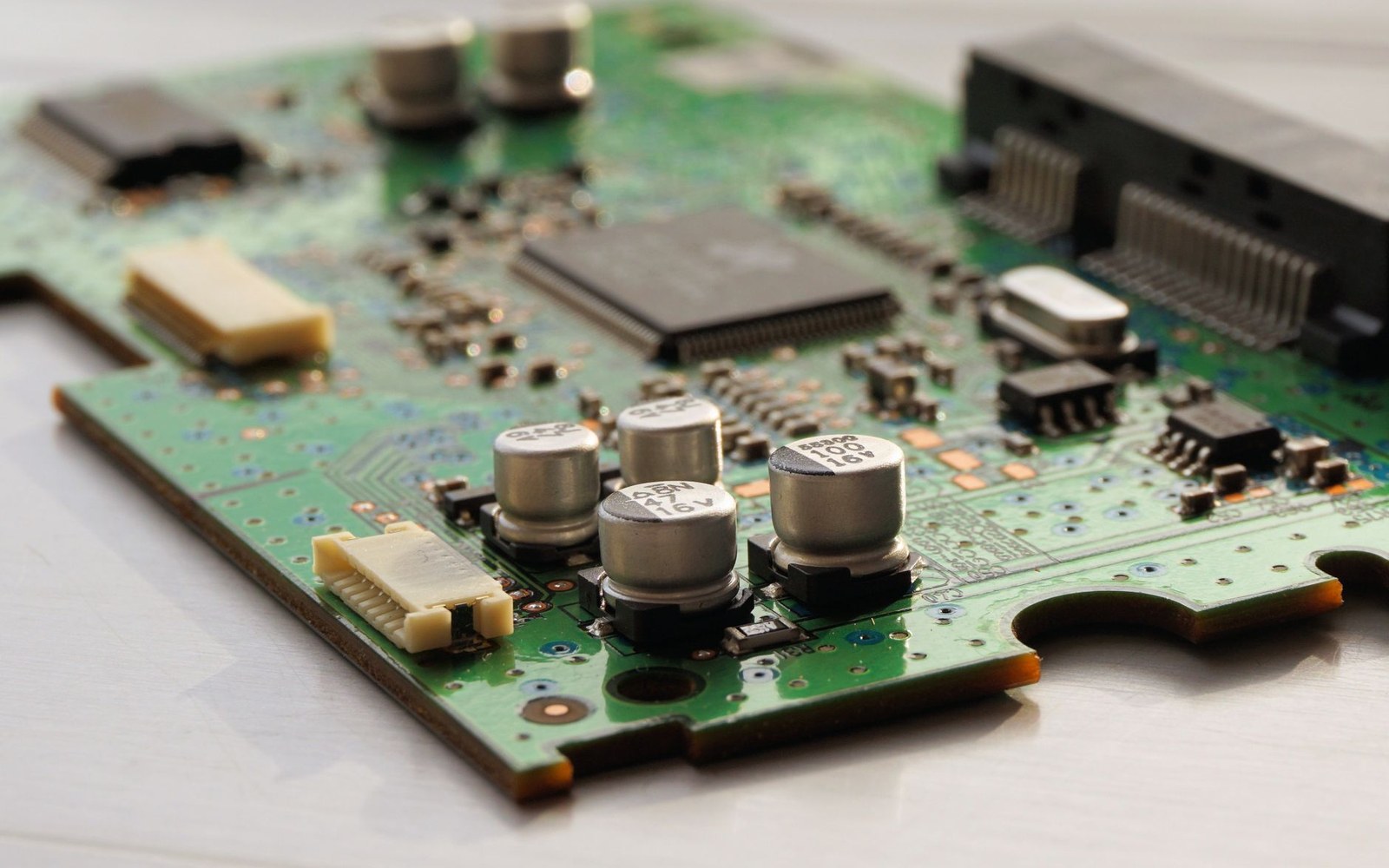 Close-up of a green circuit board with capacitors, a microchip, and connector pins