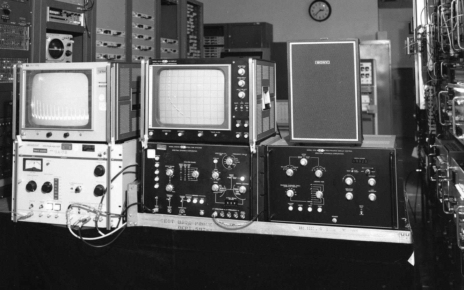 Vintage oscilloscopes and spectrum analyzer equipment with control panels sit on a lab bench