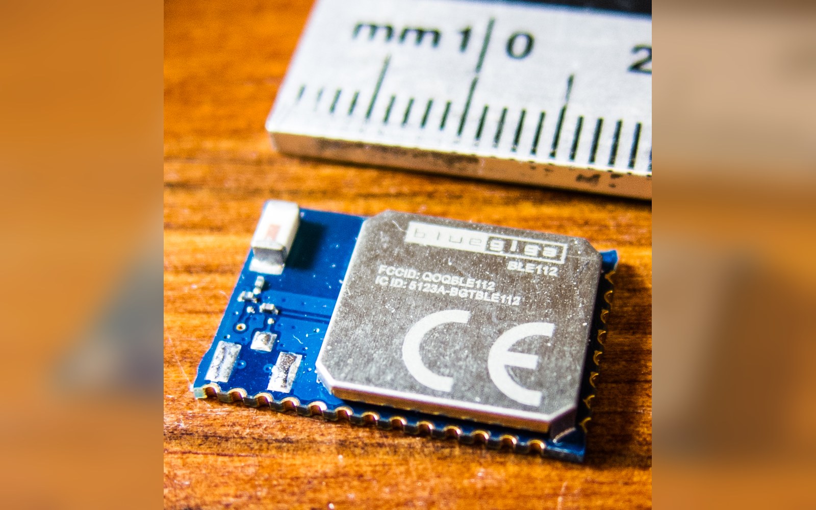A small Bluegiga BLE112 Bluetooth module on a wooden surface beside a metric ruler