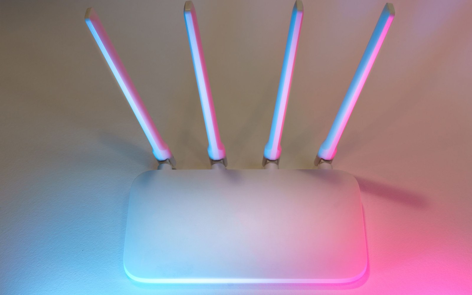A wifi router with four upright antennas lit by pink and blue ambient light
